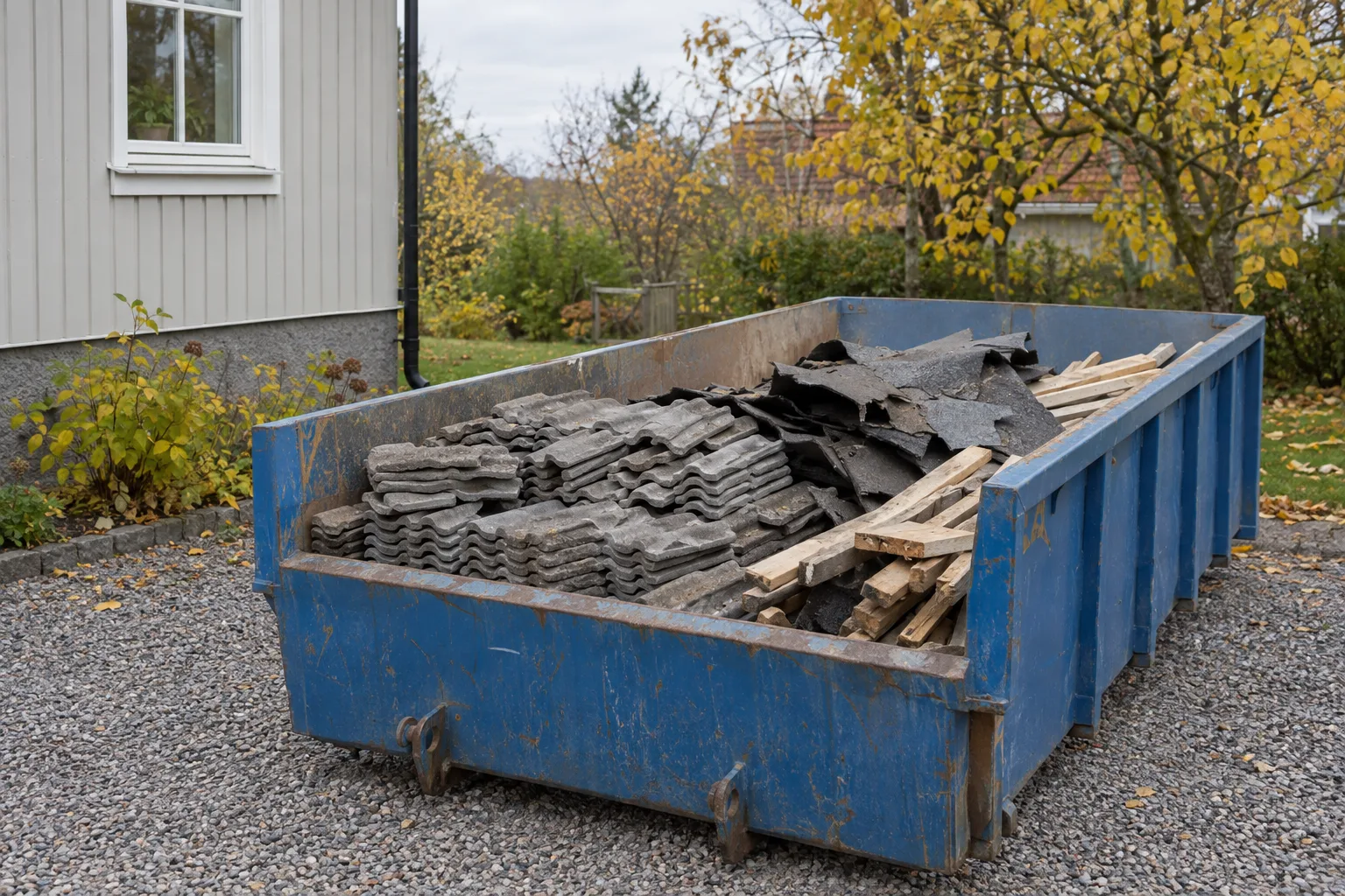 Byggcontainer på en uppfart med gamla betongpannor, riven takpapp och läkt.